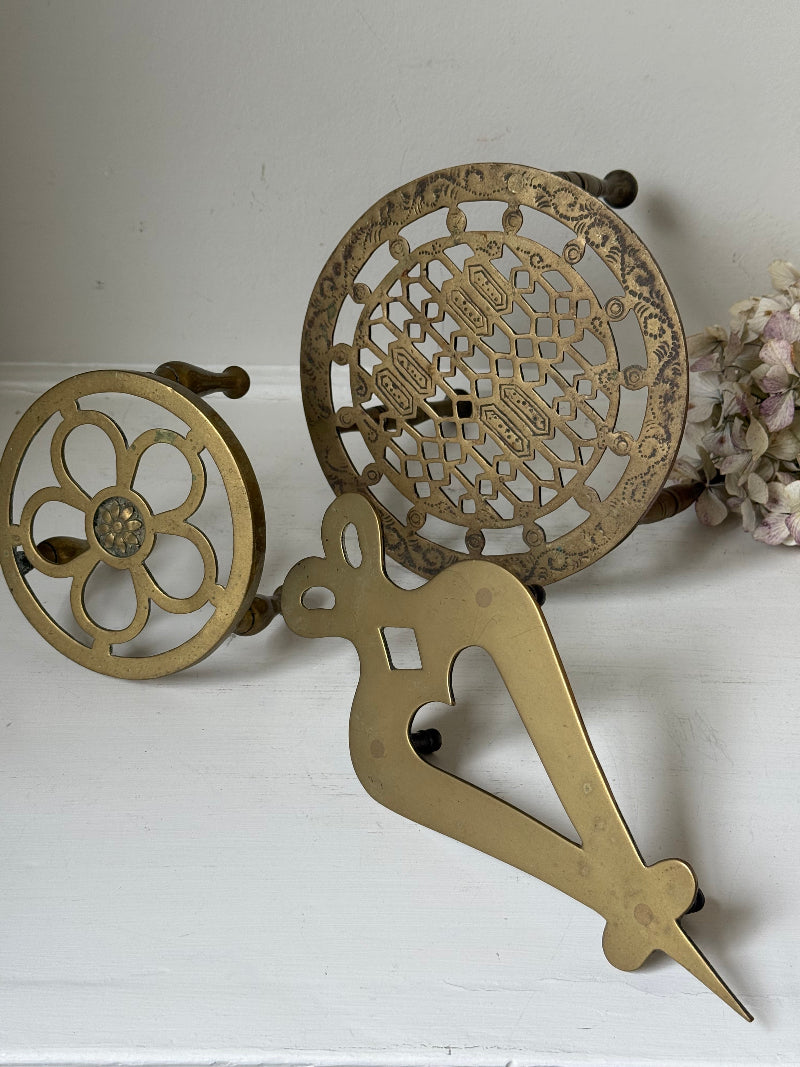 Vintage brass trivet trio with ornate cutwork designs and aged patina, photographed on a white surface