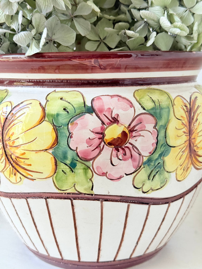 Large European hand painted floral ceramic jardinière with yellow, pink and green flowers on a white base, styled on a white surface with dried foliage.