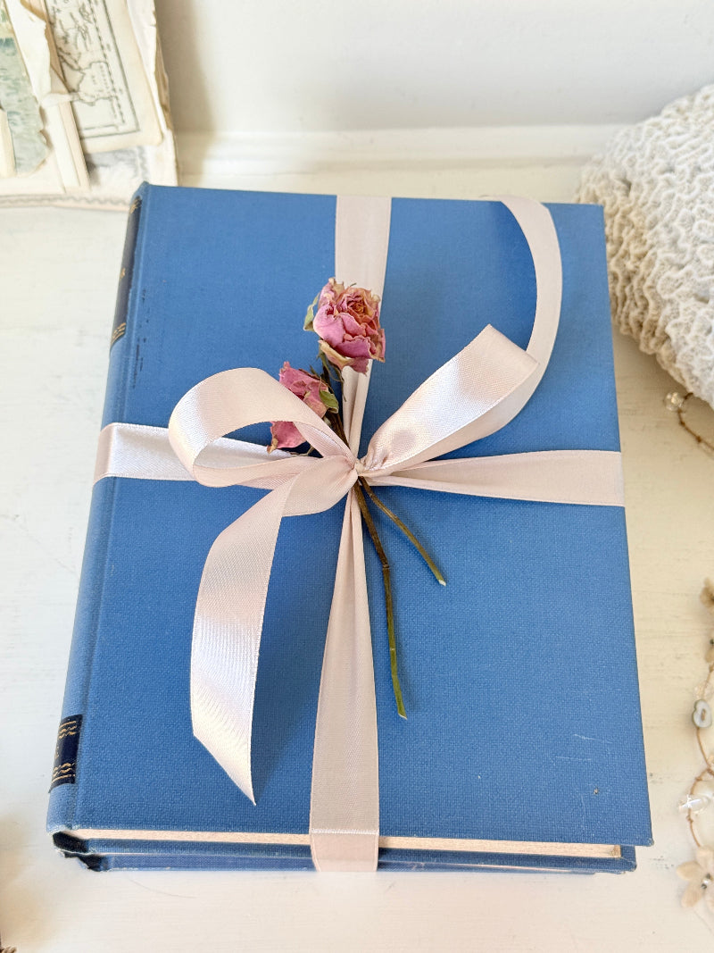 Vintage decorative blue book bundle with pale pink ribbon, dried rose detail and aged hardback covers for shelf styling