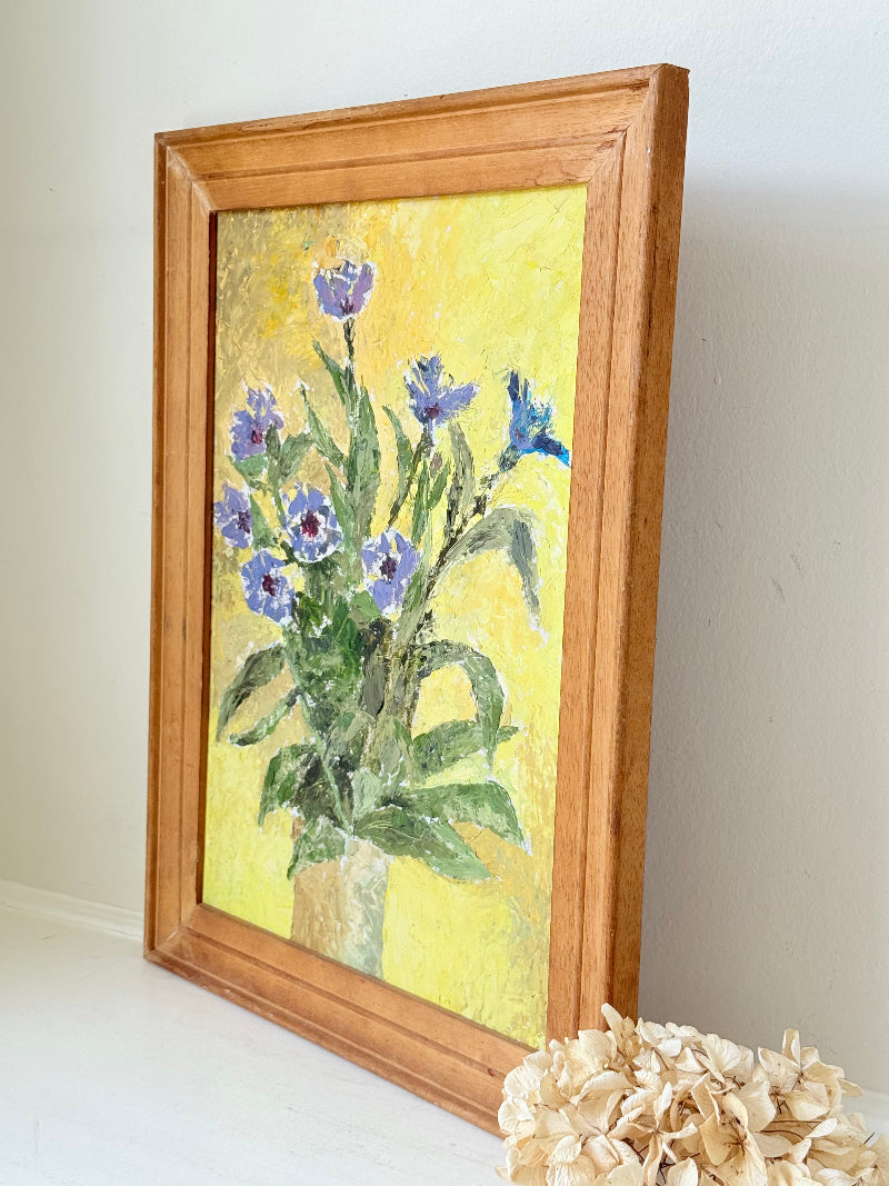 Vintage oil painting of cornflowers in a vase with yellow background in wooden frame photographed on a white surface