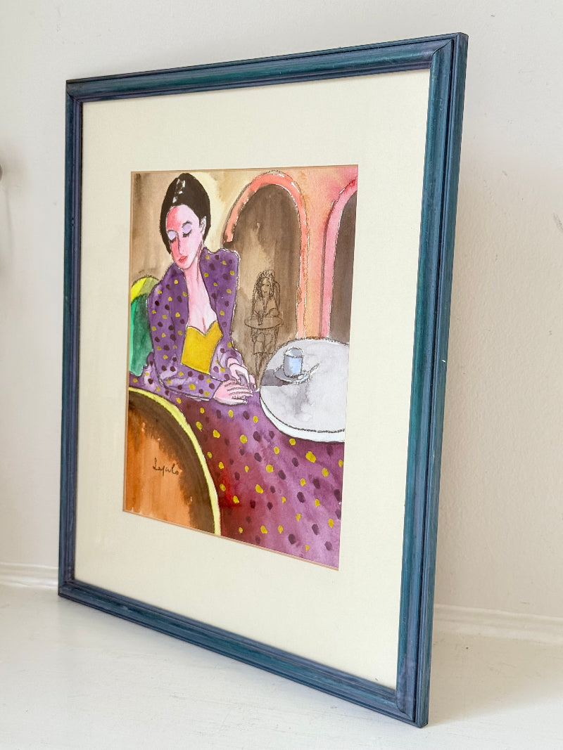Original watercolour portrait of Pamela in blue frame, vibrant interior scene, photographed on white surface