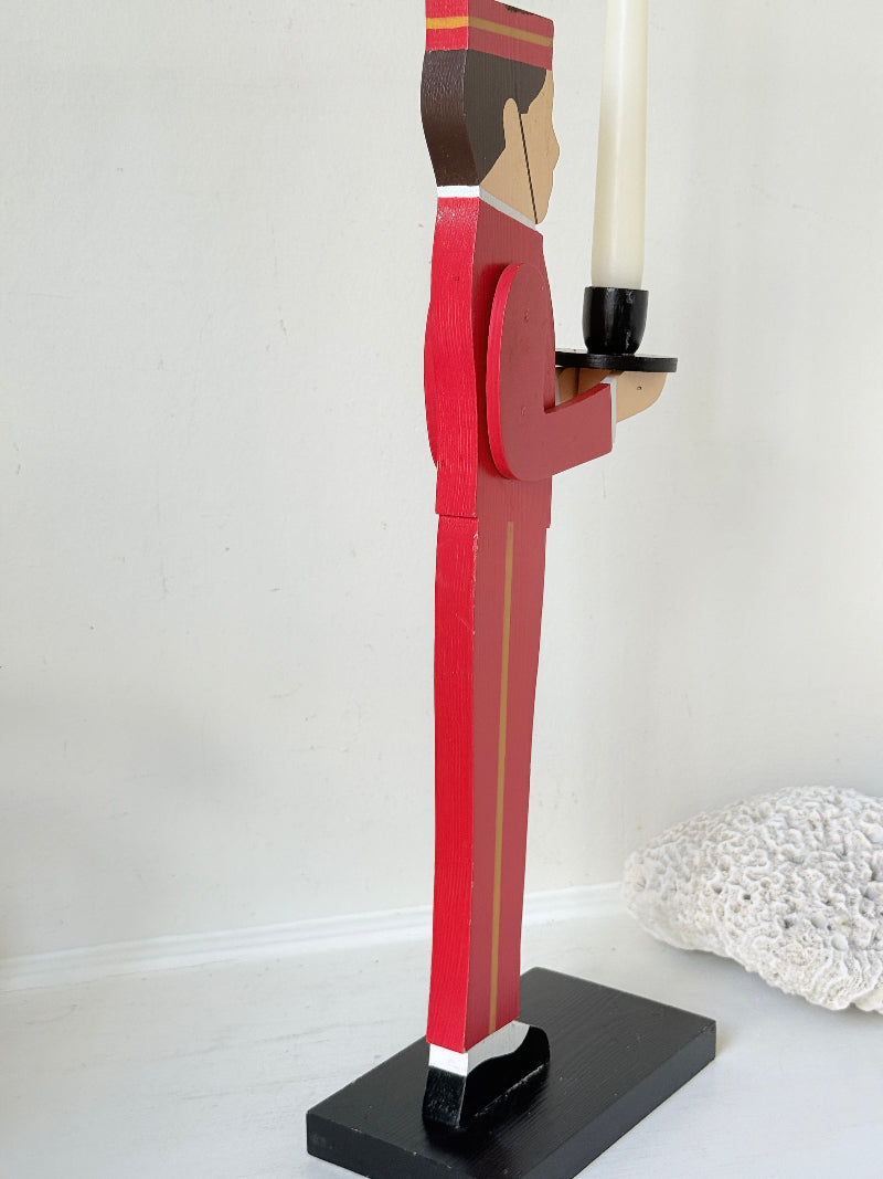 Vintage bellboy candlestick holder in red and black holding a tray with candle, photographed on a white surface