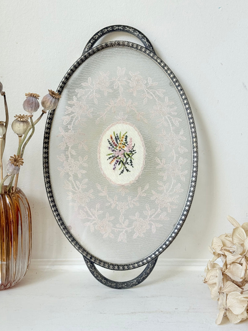 Vintage oval metal tray with pierced gallery sides, twin handles, and floral centre, photographed on white surface.