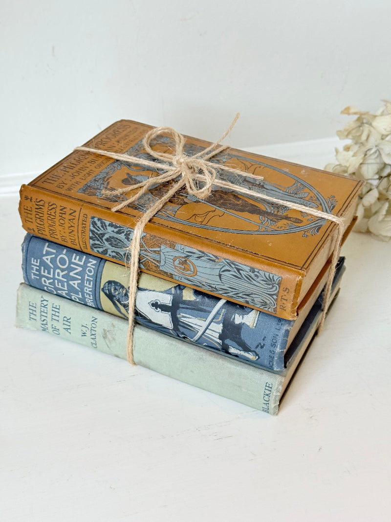 Vintage decorative book bundle in blue, grey, and ochre tied with twine, photographed on a white surface