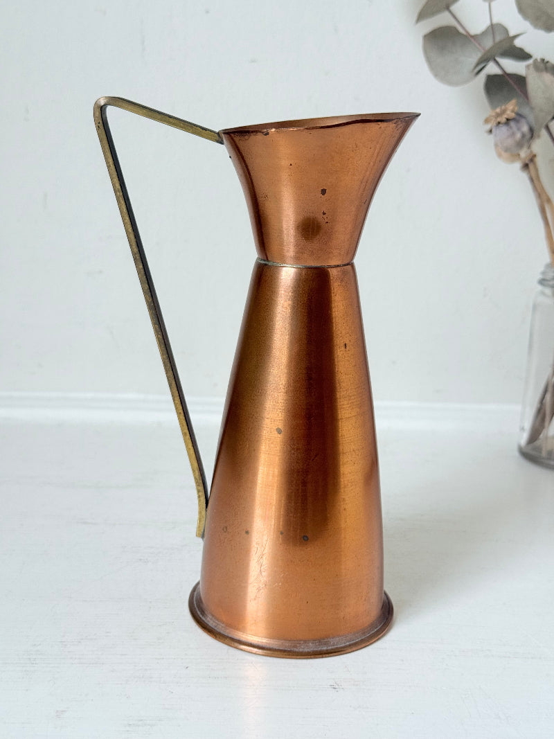 Vintage copper and brass jug with slender handle, photographed on a white surface