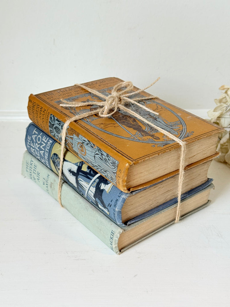 Vintage decorative book bundle in blue, grey, and ochre tied with twine, photographed on a white surface