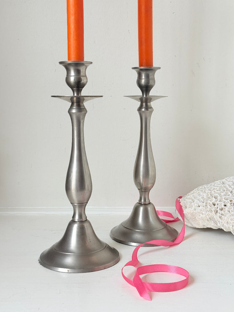 Pair of vintage pewter effect baluster candlesticks with orange taper candles styled on a white surface