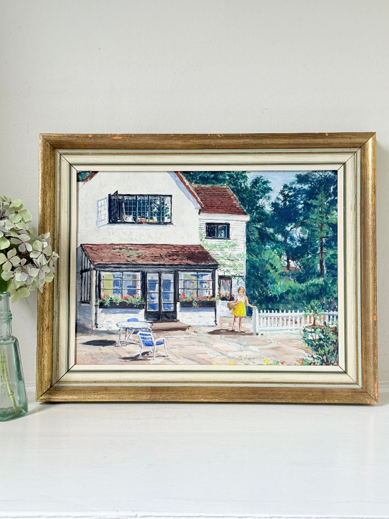 Oil on board painting of a girl in a yellow dress outside a cottage with picket fence, framed, photographed on a white surface