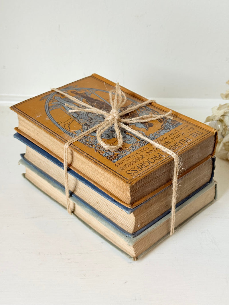 Vintage decorative book bundle in blue, grey, and ochre tied with twine, photographed on a white surface