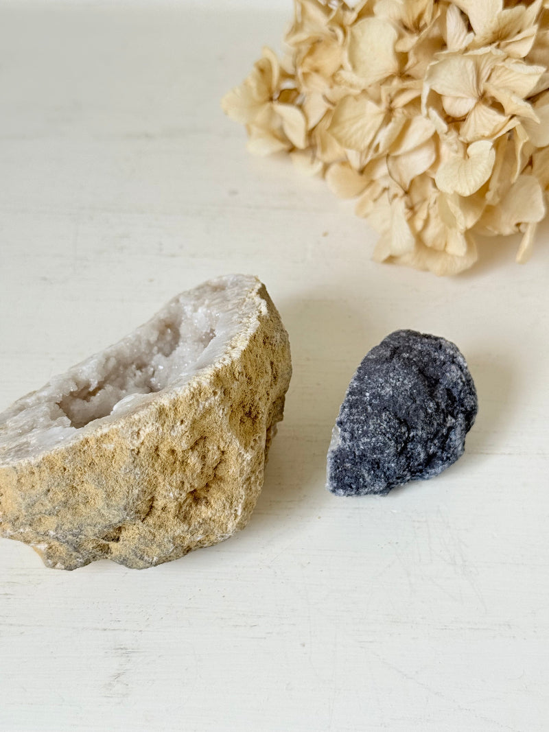 Pair of natural quartz geodes, one white and one lilac-toned, styled on a white surface with dried hydrangea