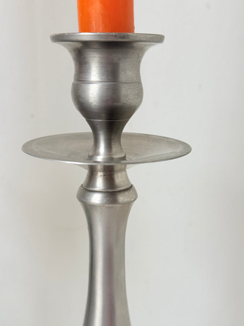 Pair of vintage pewter effect baluster candlesticks with orange taper candles styled on a white surface