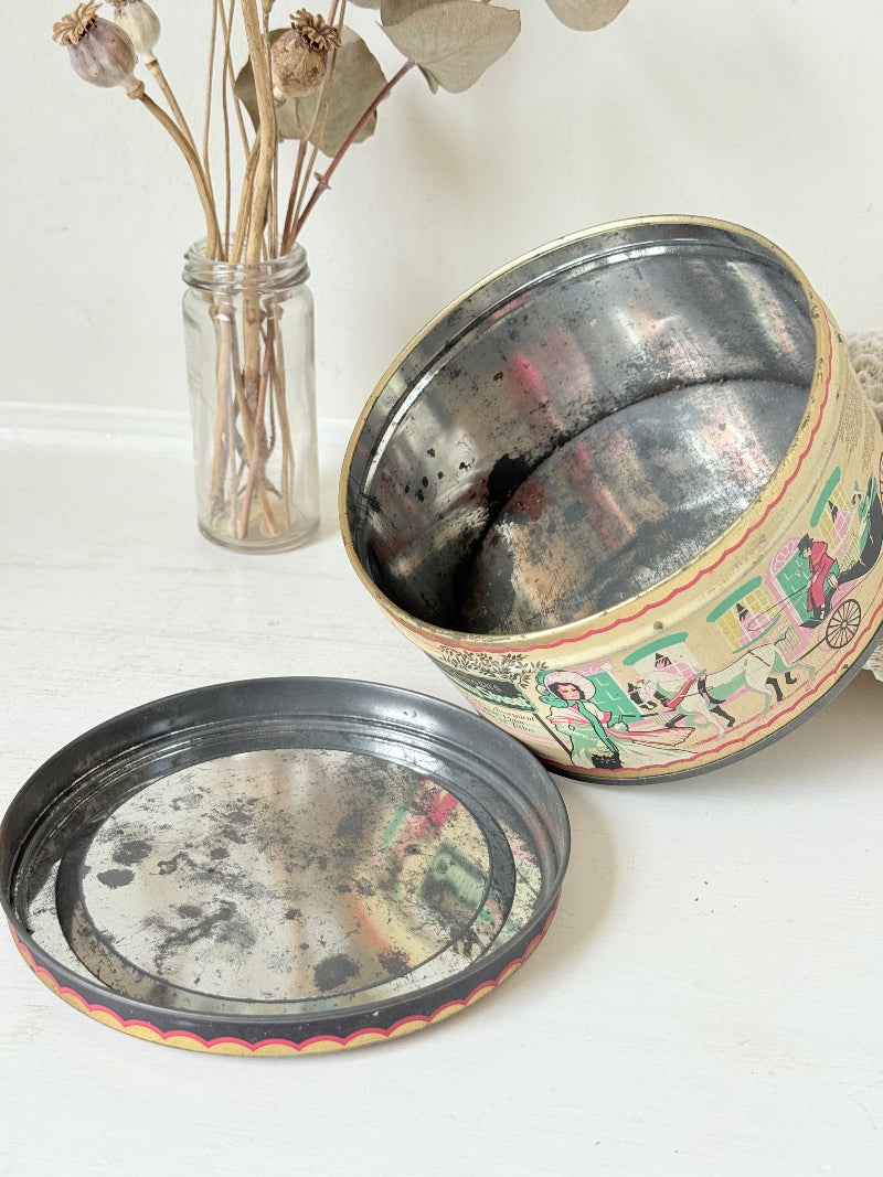 Vintage Quality Street tin from 1986 with colourful illustrated street scenes and pastel design, photographed on a white surface.