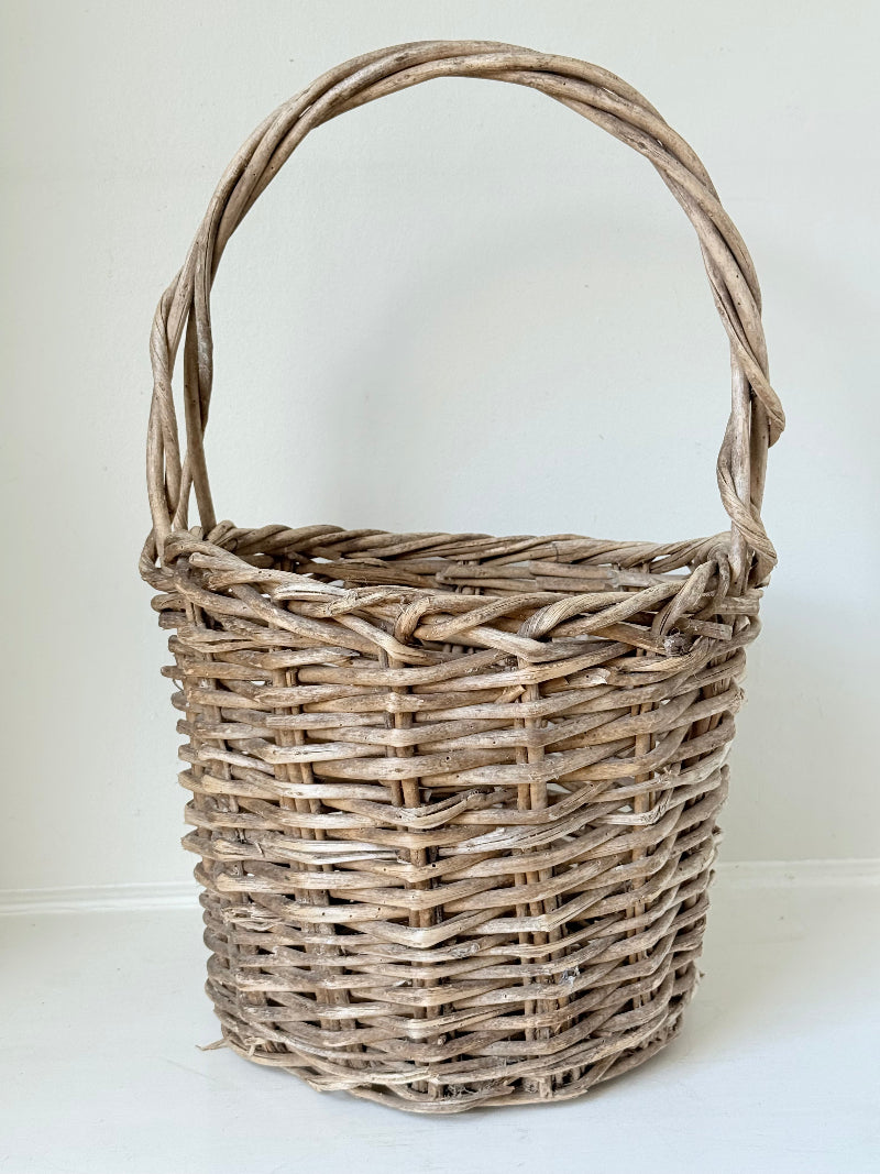 Rustic vintage wicker basket with woven handle and aged natural finish photographed on a white surface