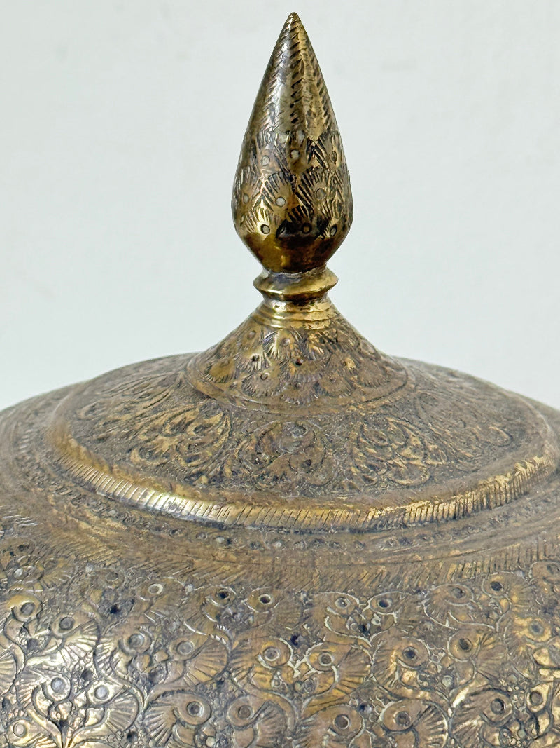 Indian Benares brass lidded jar with pointed finial and darkened interior, photographed on a white surface