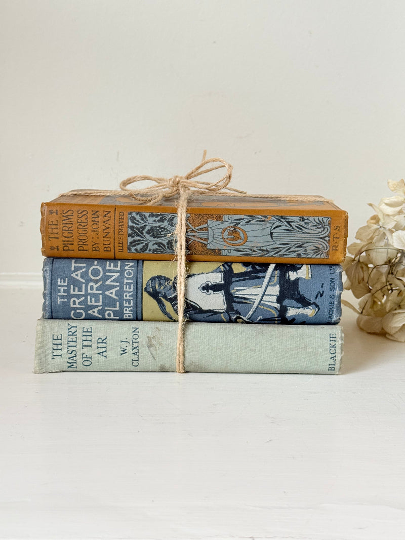 Vintage decorative book bundle in blue, grey, and ochre tied with twine, photographed on a white surface