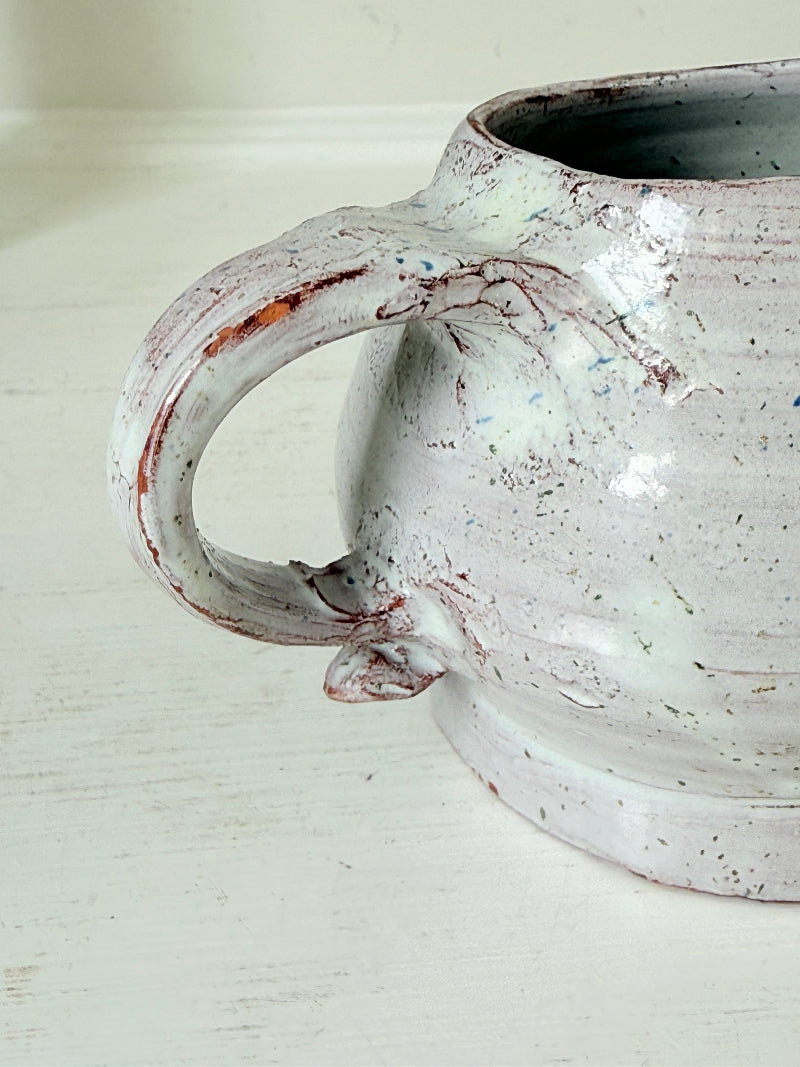 Studio pottery milk jug with soft pink and grey speckled glaze, photographed on a white surface