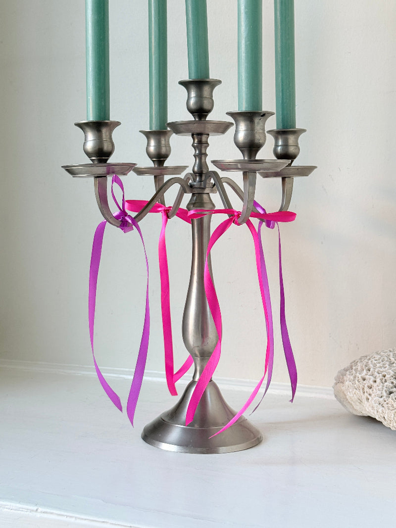 Five arm pewter style metal candelabra with aged silver finish styled with blue green taper candles on white surface
