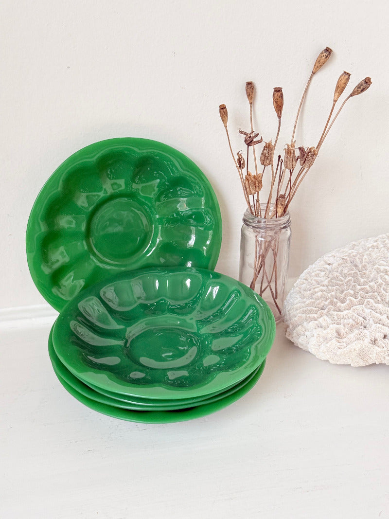set of five vintage green pressed glass plates with decorative pattern, photographed on a white surface with dried flowers