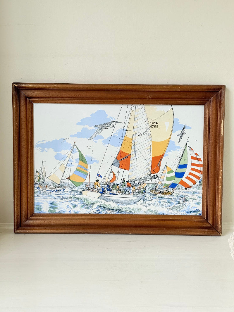 Vintage enamel artwork of sailing yachts with colourful striped sails in a regatta, framed in wood, photographed on white surface.