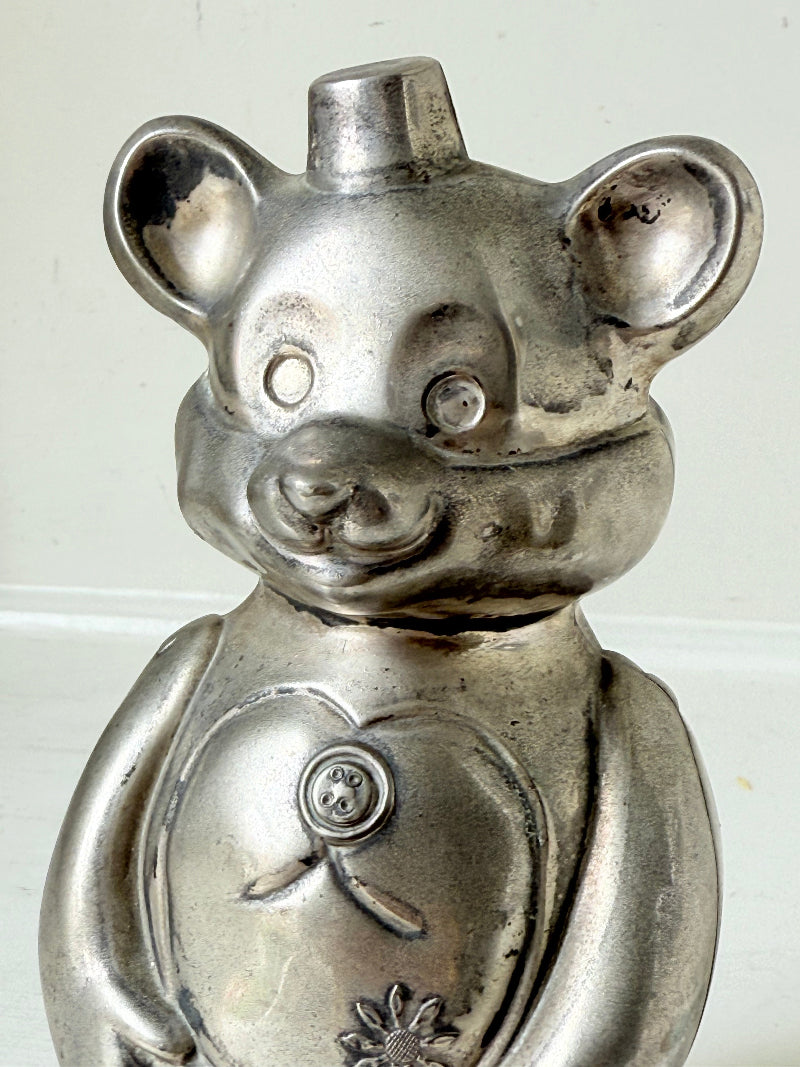 Vintage silver tone metal bear money box with coin slot on top, photographed on a white surface.