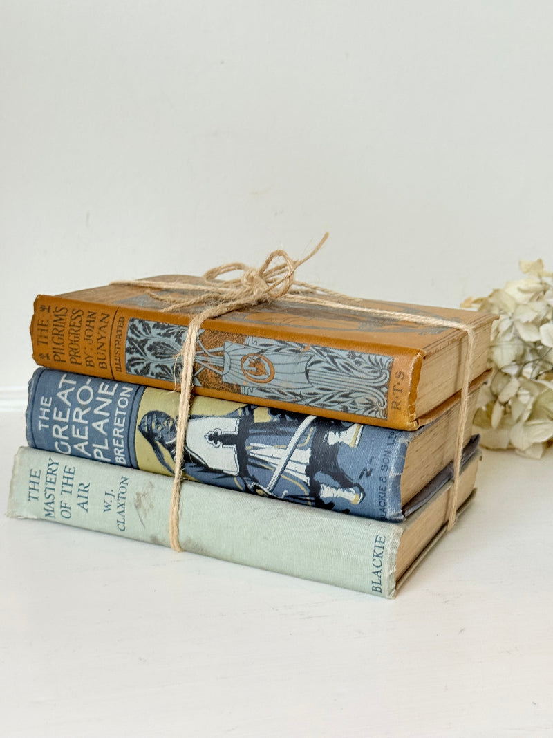 Vintage decorative book bundle in blue, grey, and ochre tied with twine, photographed on a white surface