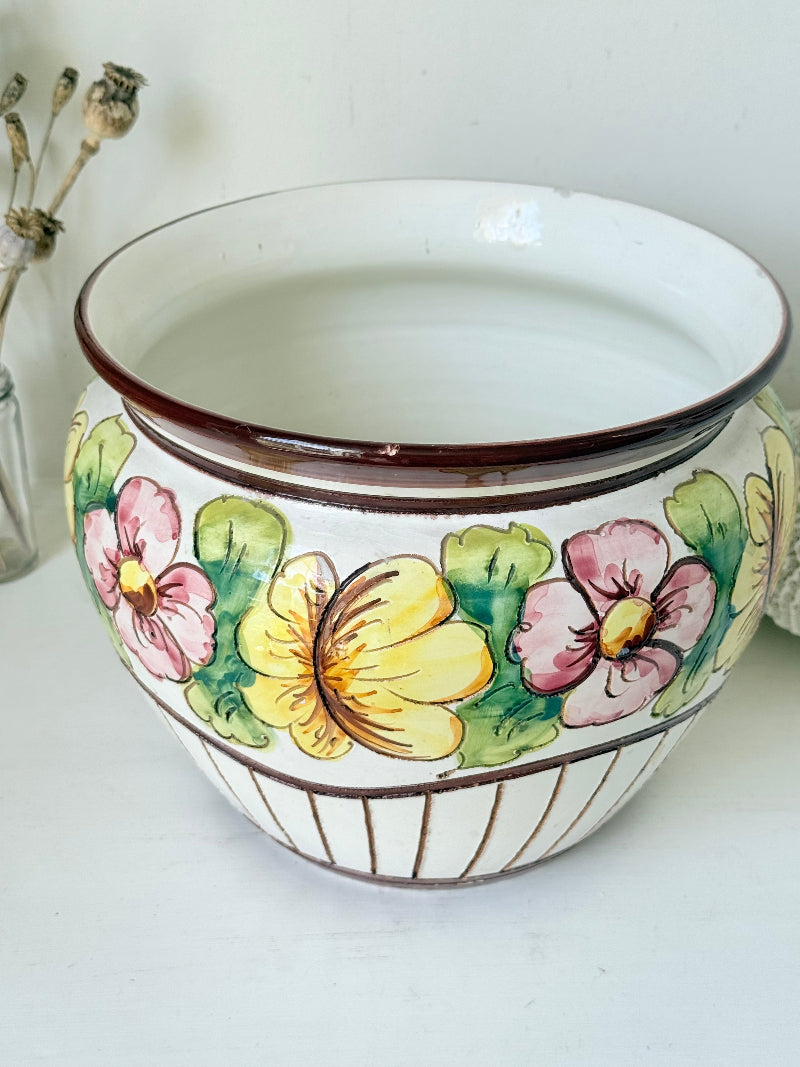 Large European hand painted floral ceramic jardinière with yellow, pink and green flowers on a white base, styled on a white surface with dried foliage.