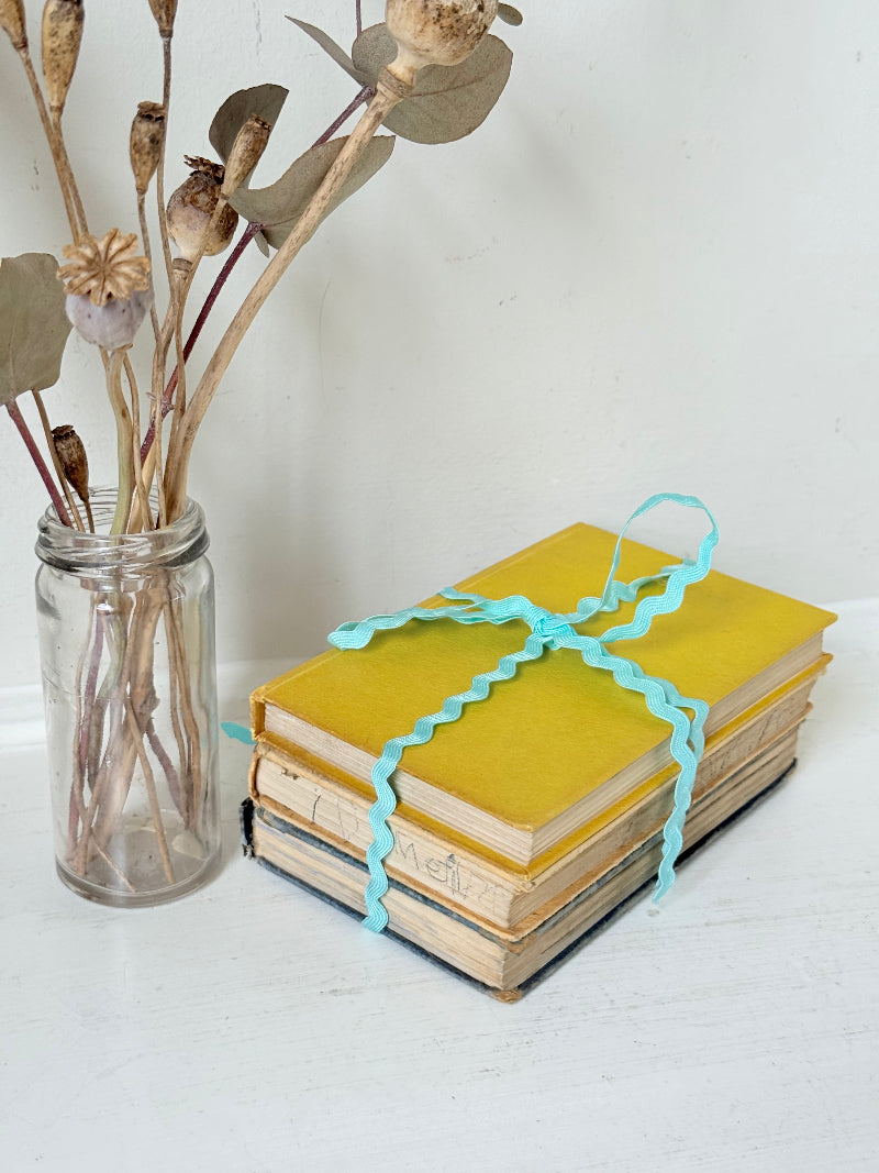 Vintage small decorative book bundle in yellow, brown and grey with turquoise ribbon, photographed on a white surface