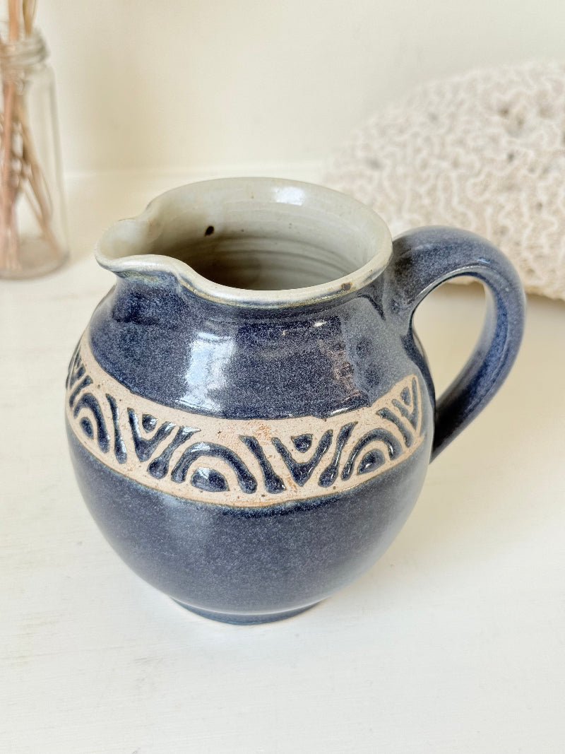 Studio pottery milk jug with deep blue glaze and cream geometric band, photographed on a white surface