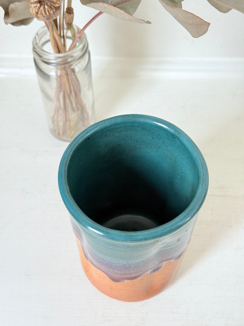 Studio pottery pen pot with teal and plum drip glaze, photographed on a white surface