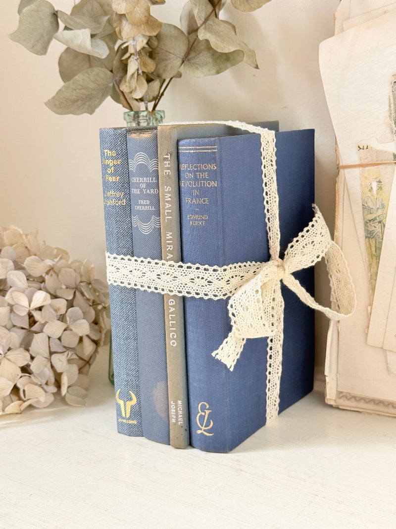 Bundle of vintage blue cloth books with gilt spines tied with ivory lace ribbon for shelf and table styling