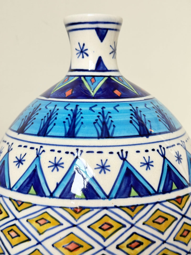 Close-up of a hand-painted ceramic vase with a white base and intricate geometric patterns in blue, yellow, and orange.