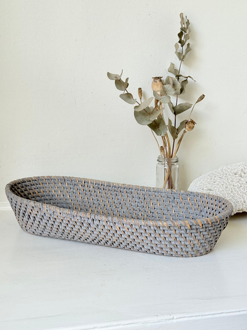 Vintage grey woven bread basket with oval shape and raised rim, photographed on white surface.