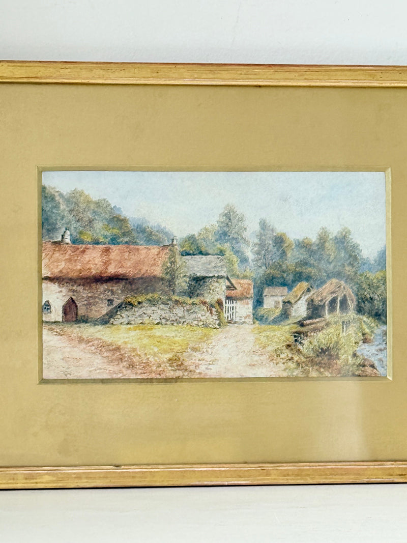 Framed vintage watercolour of countryside farm buildings with red roofs in gold frame photographed on a white surface