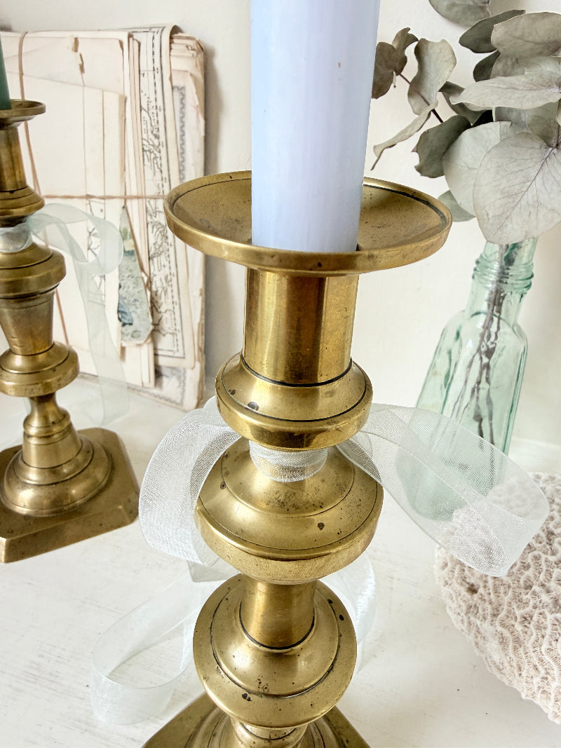 Pair of tall antique brass candlesticks with knopped columns and octagonal stepped bases holding blue and green tapers