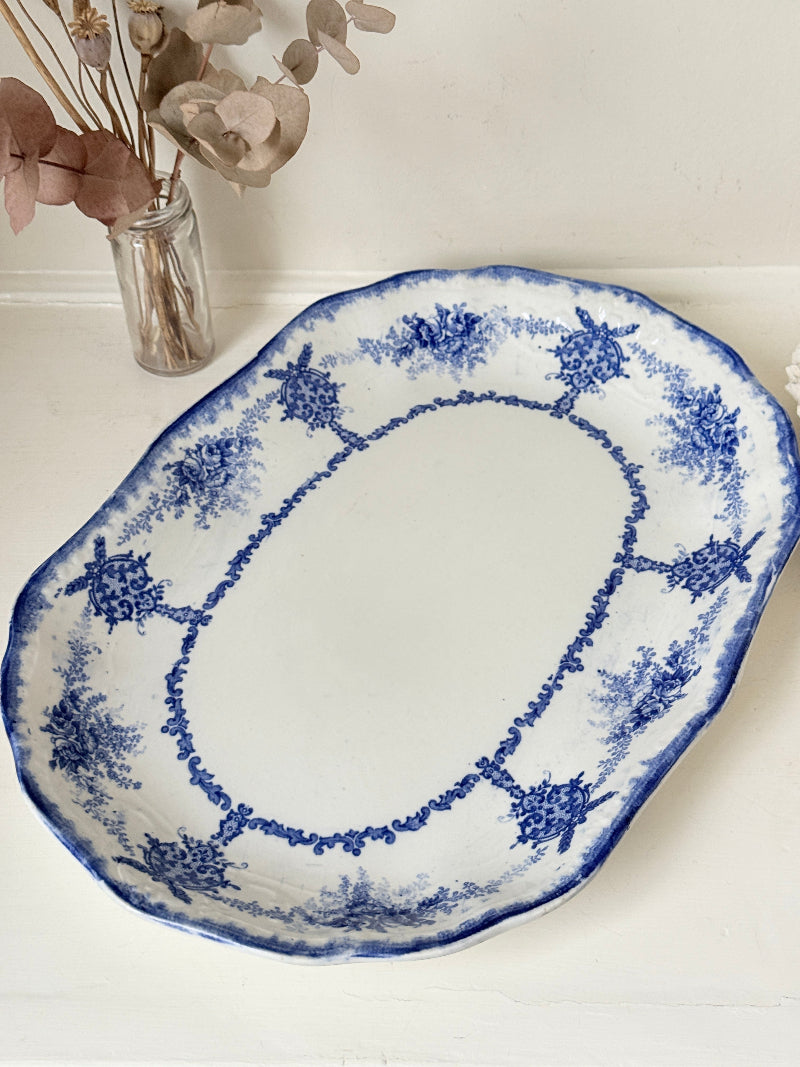 Antique oval blue and white platter with floral border photographed on a white surface