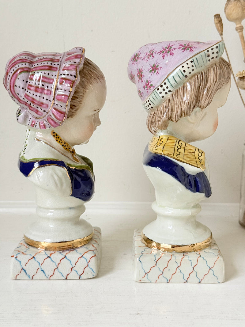 Hand painted Victorian Staffordshire ceramic children busts on white surface, photographed beside dried stems.