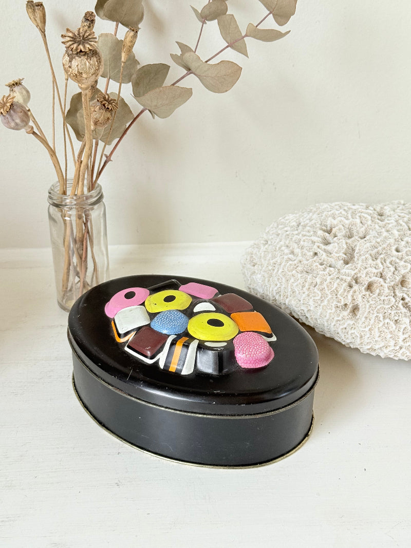 Vintage Liquorice Allsorts decorative tin with raised multicolour sweet design on black base, photographed on white surface.