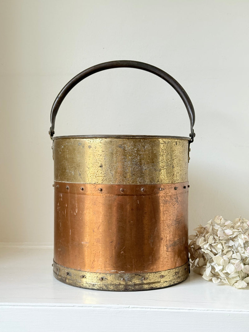Vintage copper and brass metal bin with handle, photographed on a white surface.