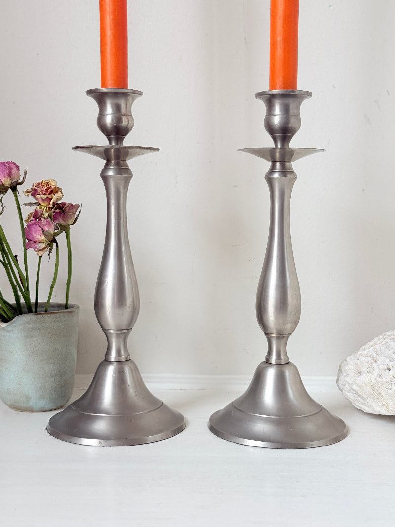 Pair of vintage pewter effect baluster candlesticks with orange taper candles styled on a white surface