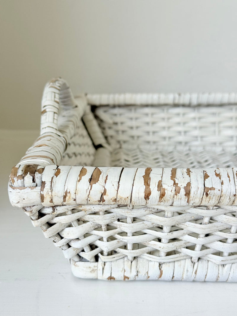 Vintage white painted wicker tray with woven handles photographed on a white surface