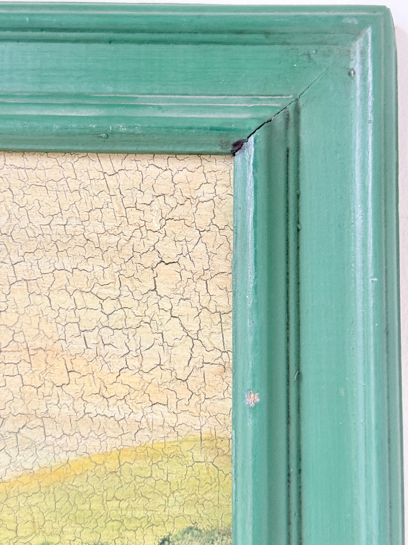 Close-up of a distressed teal-green wooden picture frame showing the corner joint and a cracked, vintage-style glass or canvas surface.