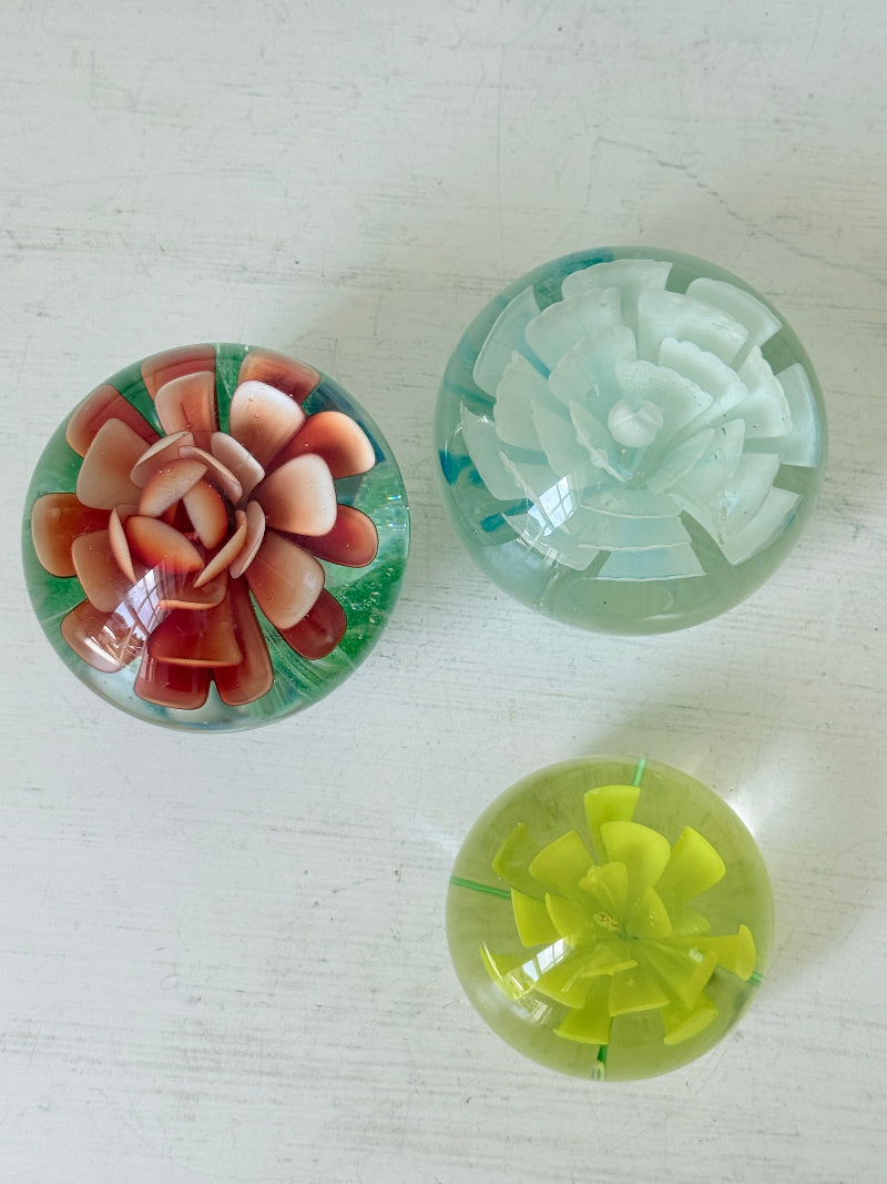 Trio of vintage glass paperweights with red flower, yellow flower and turquoise swirl decoration in clear coloured glass