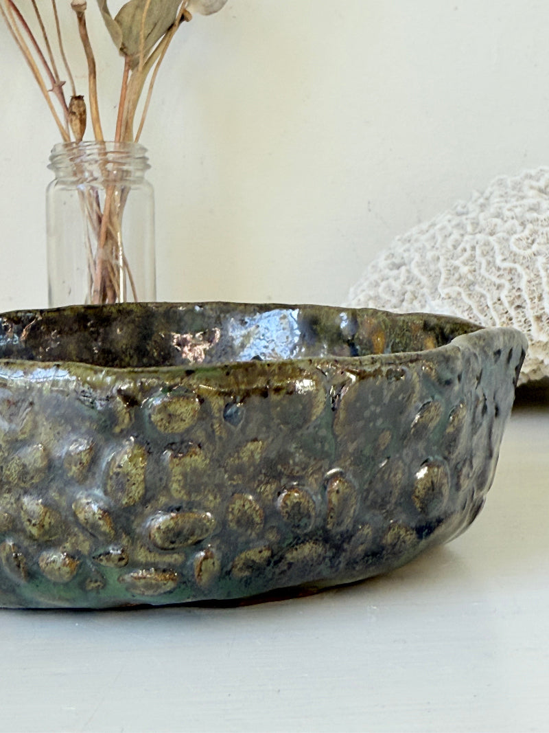 Studio pottery olive bowl with green and charcoal glaze, photographed on a white surface