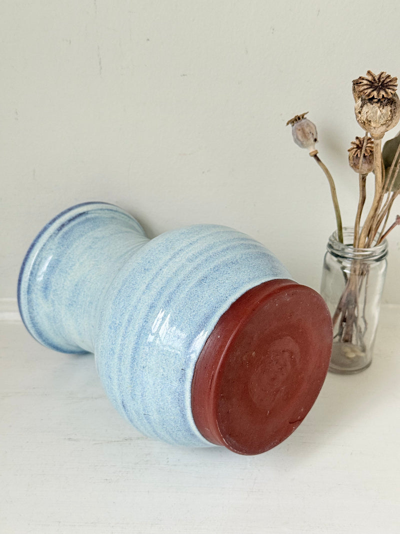 Studio pottery vase with sky blue glaze, indigo rim, and natural red clay base, photographed on a white surface