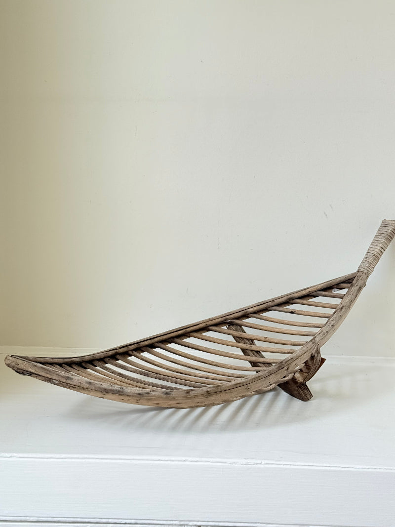 Large curved woven basket with slatted sides and repaired plywood base photographed on a white surface