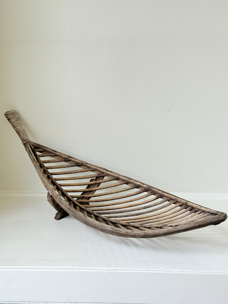 Large curved woven basket with slatted sides and repaired plywood base photographed on a white surface