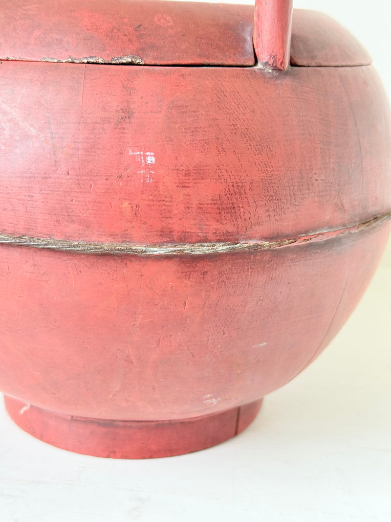 Vintage red painted wooden basket with tall curved handle and domed lid photographed on a white surface