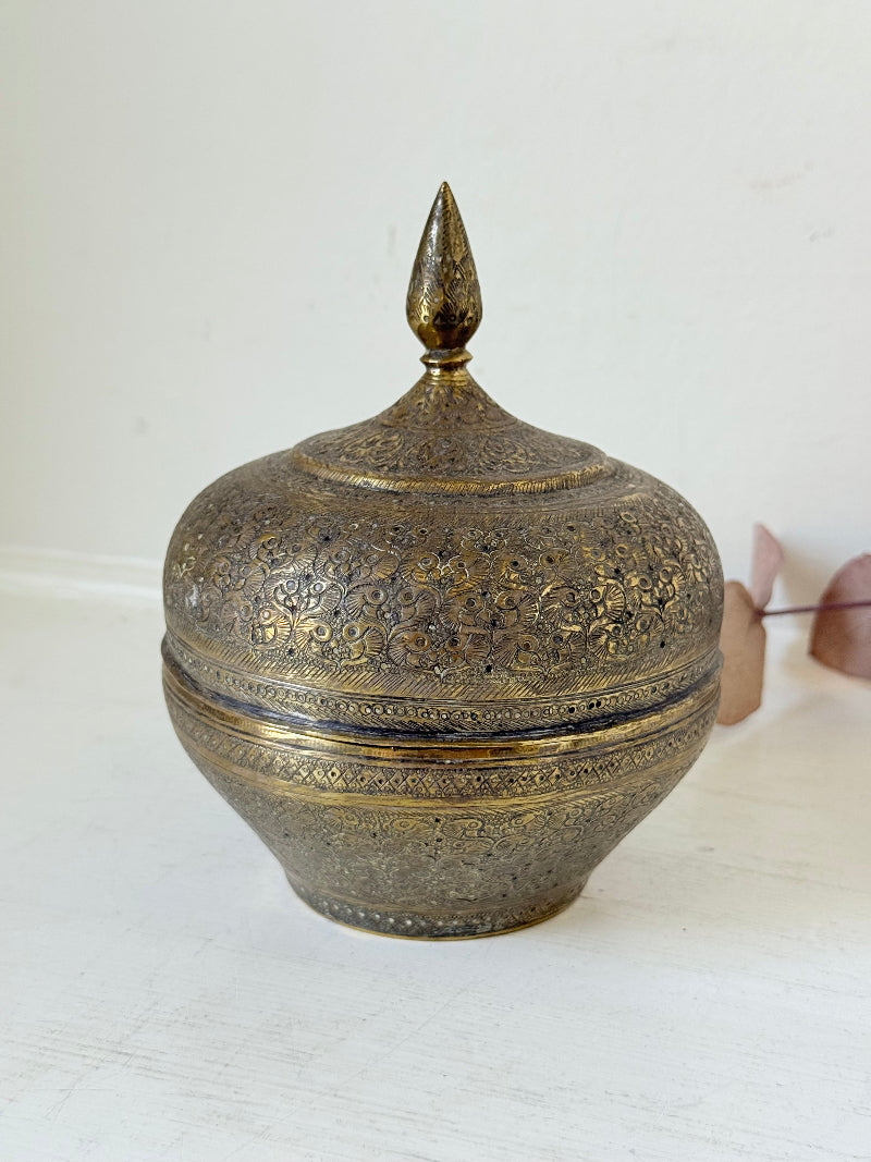 Indian Benares brass lidded jar with pointed finial and darkened interior, photographed on a white surface