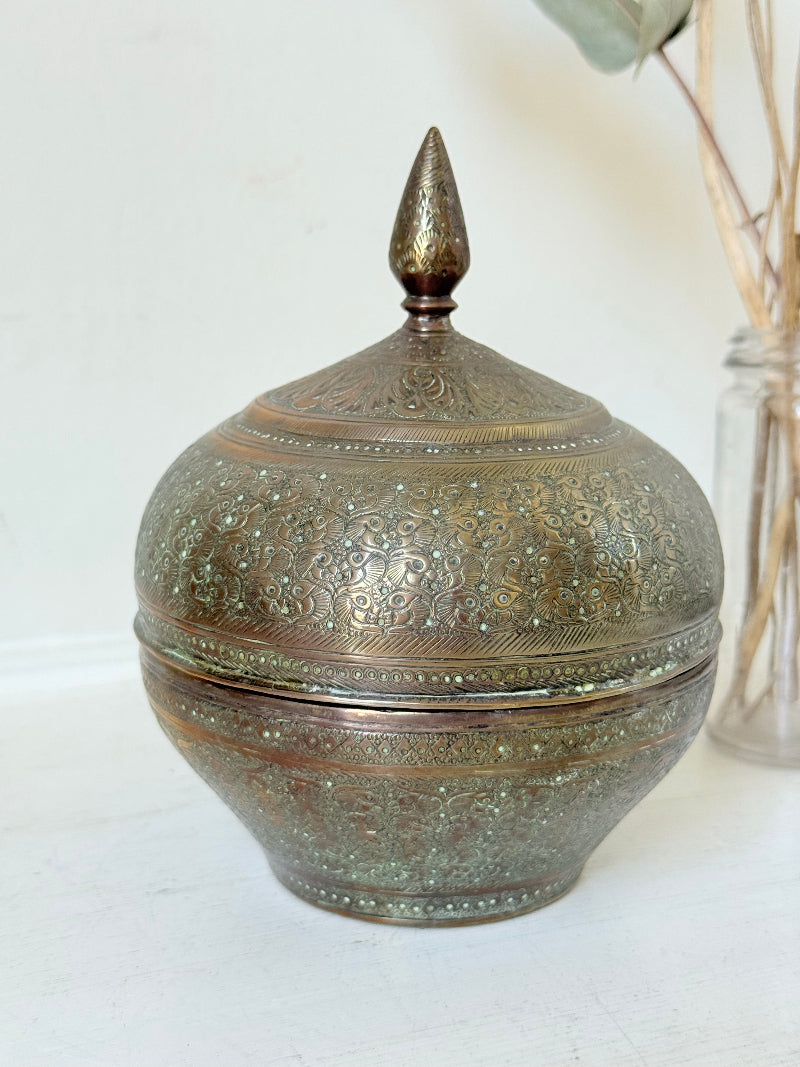 Indian Benares brass lidded jar with floral engraving and finial, photographed on a white surface