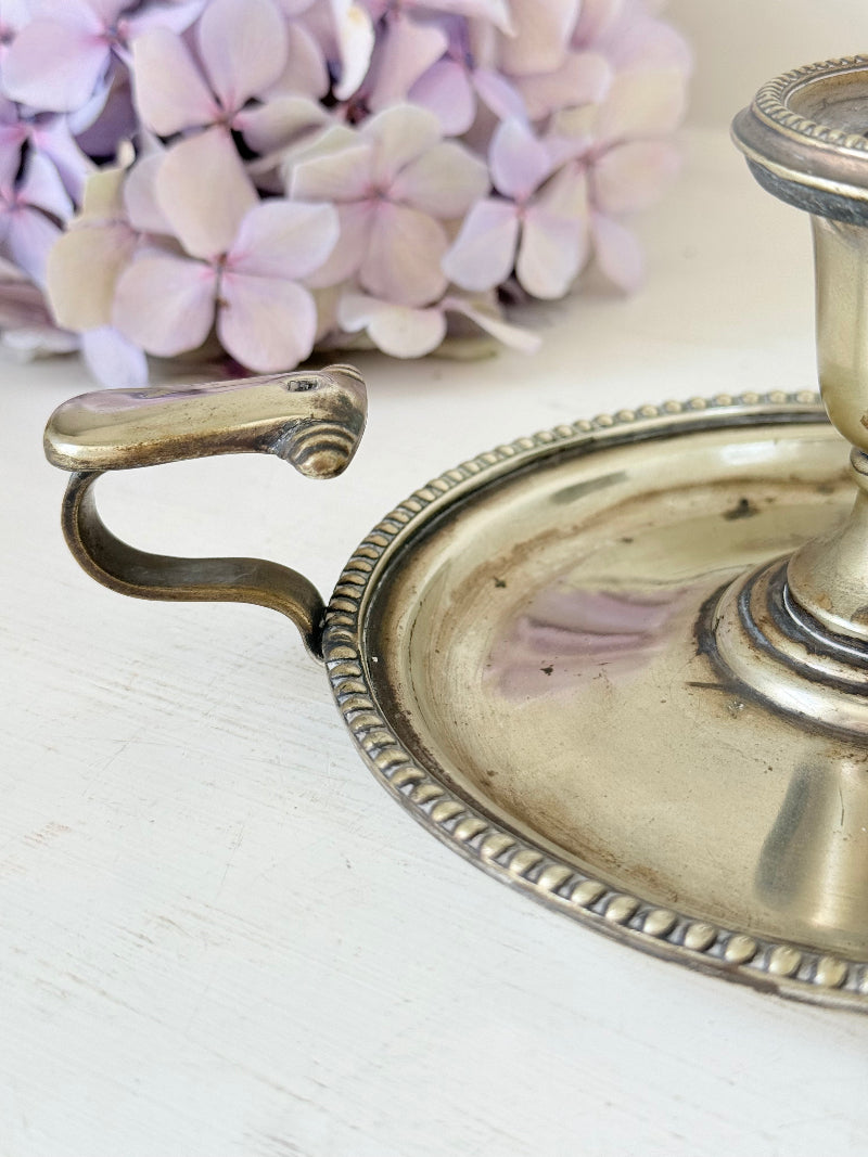 Antique silver plate chamberstick with handle, photographed on a white surface beside pink hydrangeas and vintage books